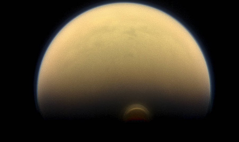 As winter sets in at Titan’s south pole, a cloud system called the south polar vortex (small, bright “button”) has been forming, as seen in this 2013 image. Credits: NASA/JPL-Caltech/Space Science Institute
