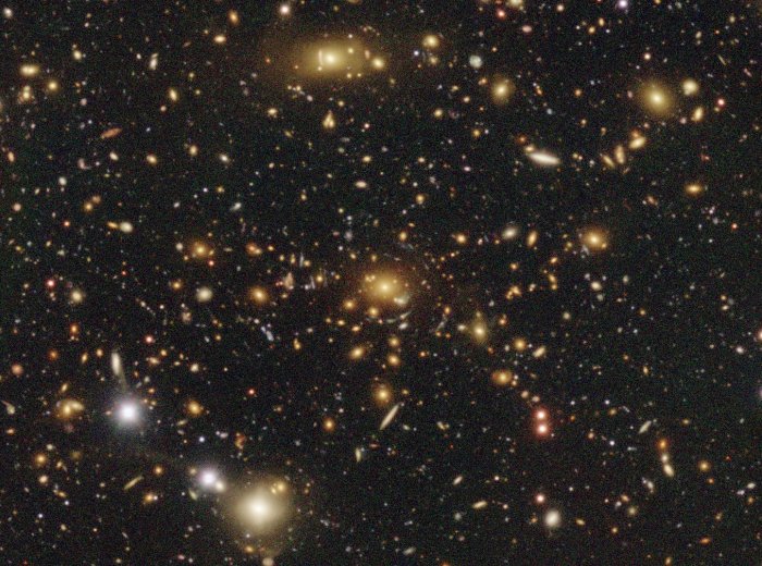 Hyper Suprime-Cam image of a location with a highly significant dark matter halo detected through the weak gravitational lensing technique. This halo is so massive that some of the background (blue) galaxies are stretched tangentially around the center of the halo. This is called strong lensing. Credit: NAOJ