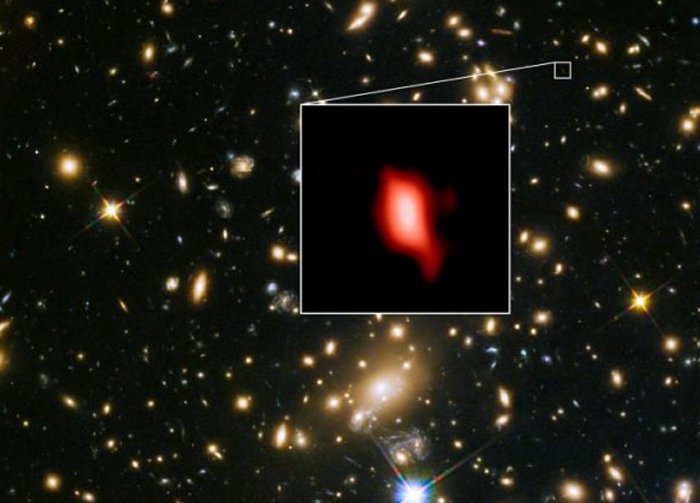 This image shows the galaxy cluster MACS J1149.5+2223 taken with the NASA/ESA Hubble Space Telescope; the inset image is the very distant galaxy MACS1149-JD1, seen as it was 13.3 billion years ago and observed with ALMA. Here, the oxygen distribution detected with ALMA is depicted in red. Credit: ALMA (ESO/NAOJ/NRAO), NASA/ESA Hubble Space Telescope, W. Zheng (JHU), M. Postman (STScI), the CLASH Team, Hashimoto et al.